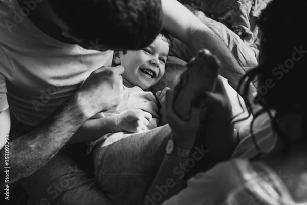 Fototapeta Close up portrait of a little smiling blond boy. He is playing with parents. Mother, father are sharing good emotions while relaxing at home Natural light, terracotta bed linen. Happy family at home.