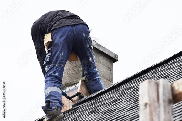 Obraz Roofer construction worker repairing chimney on grey slate shingles roof of domestic house, sky background with copy space.
