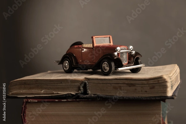 Fototapeta An old toy retro car stands on a stack of old books. Vintage effect