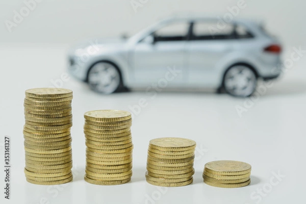 Fototapeta Lower interest rates; stacked coins, out-of-focus car in the background.