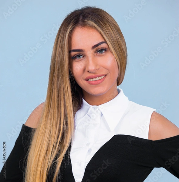 Obraz portrait Attractive young blonde model posing in trendy dress isolated at blue studio background. Beautiful girl standing in trendy clothing looking at camera