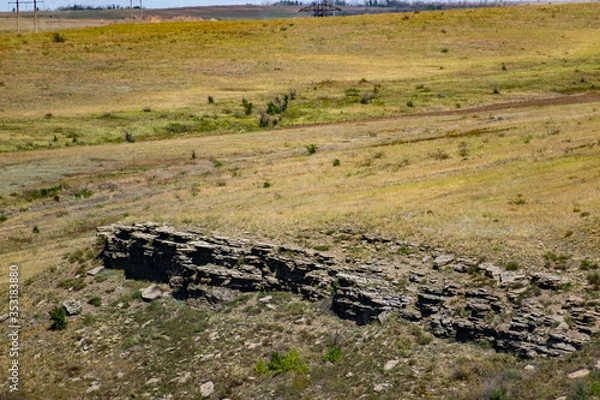 Fototapeta An unusual view in the Rostov region of the stony Zaitsev rocks, around green deciduous trees, dry yellow grass, blue sky and Sunny warm summer light
