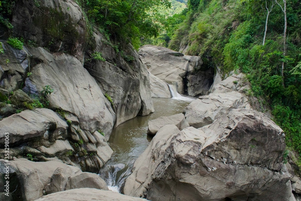 Fototapeta Small waterfall dropping to a stream at the center of huge rock formations. Rock formations caused by water flowing streams of water