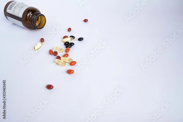Fototapeta Mix of colorful vitamins and supplements for health and sport in the form of capsules on a white background next to a brown glass jar of vitamins.