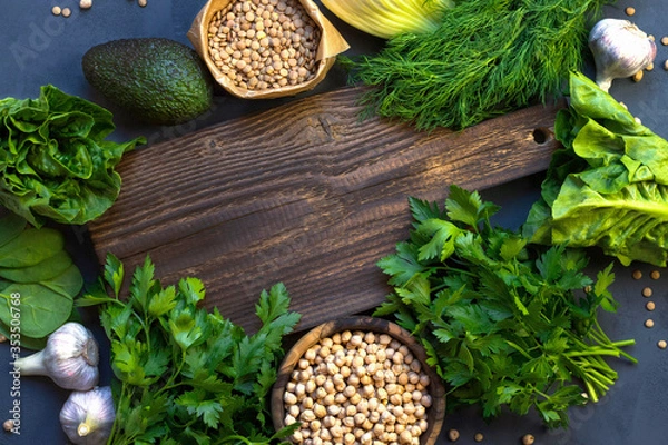 Fototapeta Vegetarian cooking concept of green fresh vegetables. A wooden board and next to a salad, parsley, avocado, chickpeas and lentils. Place for text