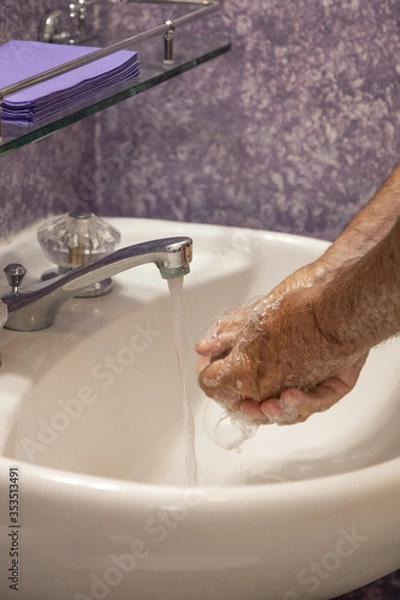 Fototapeta Man soaping hands in bathroom sink with running water from faucet