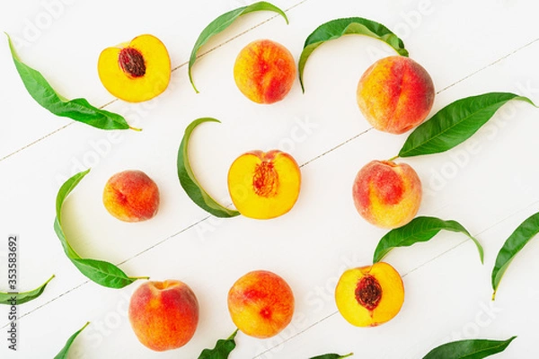 Obraz Peaches with leaves on white wooden background with peach in halves. Flat lay composition with ripe juicy peaches. Harvest of peaches for food or juice. Top view fresh organic peach fruit