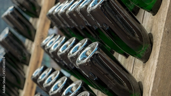 Fototapeta Wooden racks with filled green bottles of champagne during traditional bottle fermentation waiting for the next manual bottle rotation to proceed with the maturation process. 