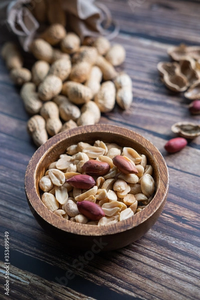 Fototapeta Peanuts in a wooden bowl on wooden background. Healthy snack. Vertical picture.