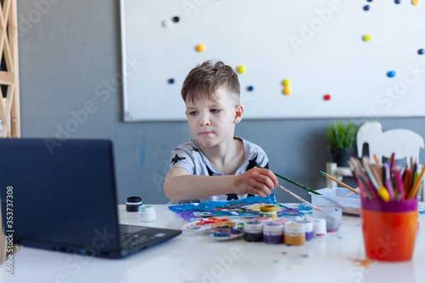 Obraz boy paints, online drawing classes, gray Tshirt with stars, laptop on the table