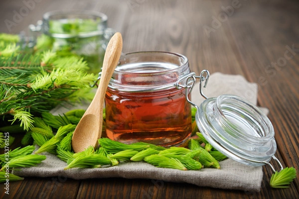 Fototapeta Jar of  jam, syrup or honey from fir buds and needles, twigs of fir tree on wooden table. Making spruce tips jam at home.