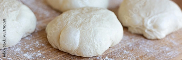 Fototapeta A round pieces of homemade white dough for pizza, bread or baking goods on a wooden cutting board. Small pieces of dough ready to be baked. Healthy natural family food. Side view, daylight, home 