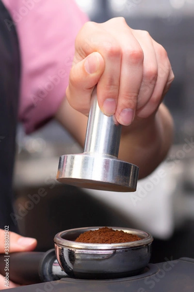 Fototapeta close-up photo of female hands holding a metal tamper and a portafilter with coffee in a coffee shop. barista preparing for pressing ground coffee for brewing espresso. vertical photo