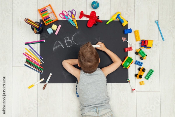 Obraz Kid draws on a black sheet of paper. Boy writing a letter