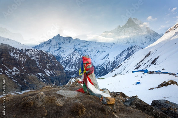 Fototapeta Colorful Flags Mark the Base Camp of Annapurna in Nepal with Machapuchare in the Sunrise Haze with Clouds