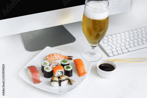 Obraz Assorted sushi and rolls near the computer. Eating at the workplace. Relax at home with a glass of beer.