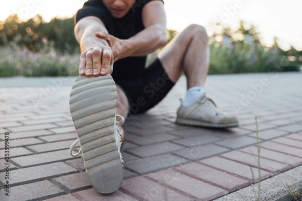 Fototapeta Man does stretching exercises on paving tile in outdoor park