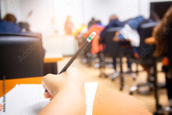Fototapeta Hands university student holding pen writing /calculator doing examination / study or quiz, test from teacher or in large lecture room, students in uniform attending exam classroom educational school.