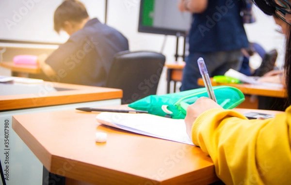 Fototapeta Hands university student holding pen writing /calculator doing examination / study or quiz, test from teacher or in large lecture room, students in uniform attending exam classroom educational school.