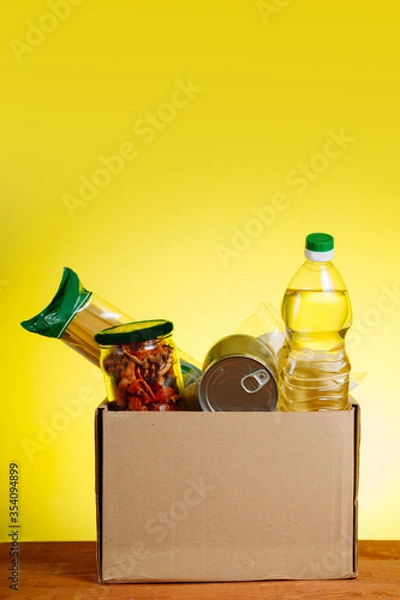 Fototapeta Food Donation concept. Donation Box With food For Donation On Yellow Backround. Assistance To The Elderly In The Context of The Coronavirus Pandemic. Vertical shot
