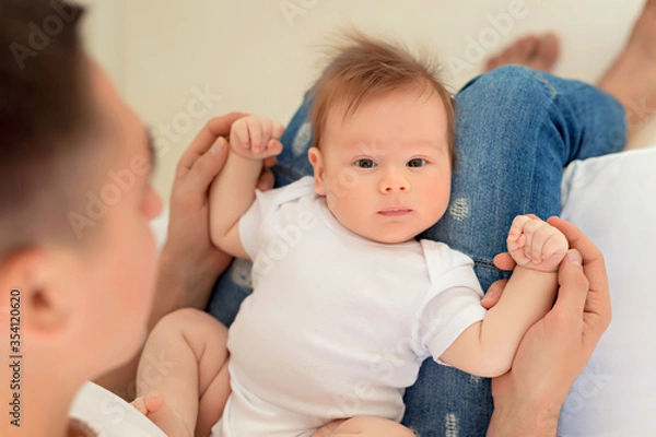Obraz Father and baby son play on a white bed in a sunny bedroom. Parent and little child are resting at home. Family having fun together.