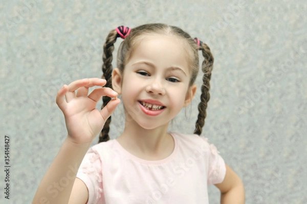 Obraz little girl smiles and holds a lost milk tooth in her hands, selective focus, pastel colors