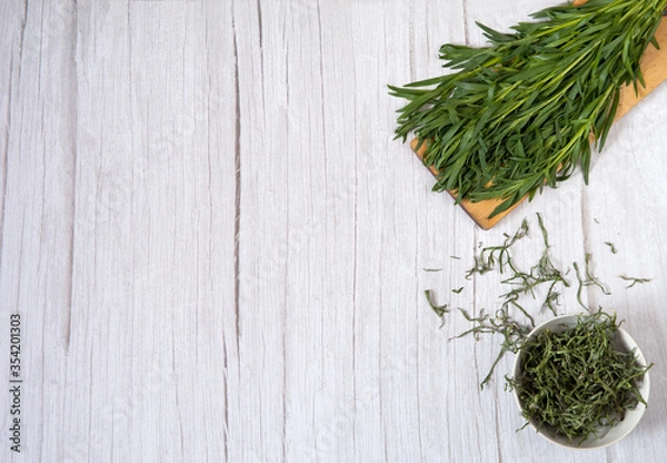 Obraz Drying of greens with preservation of vitamins. A bunch of fresh tarragon on a cutting board and a cup of dried tarragon on a light wooden background. Free space.