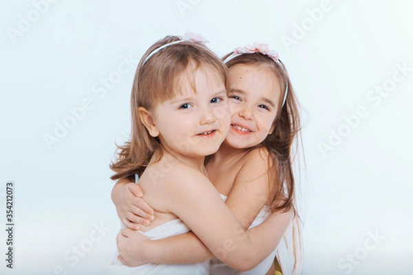 Fototapeta two little happy girls smiling on white background. Portrait of children hugging. The concept of relationships in the family, friends, sisters, couple in love. Copy space