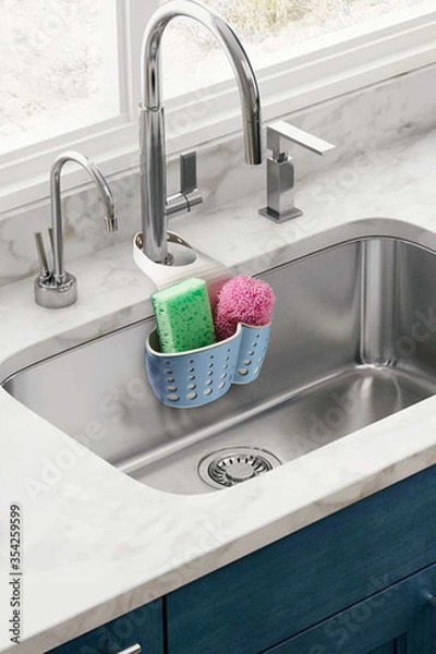 Fototapeta Detailed shot of a blue plastic sponge holder with an adjustable strap. The kitchen organizer with green and pink sponges is hanging on the chrome faucet over the kitchen sink. 