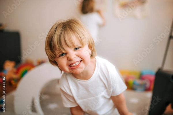 Obraz little blond boy laughs looking at camera at home. fun at home family at home