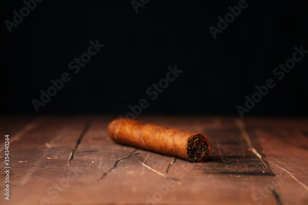 Obraz A beautiful fresh Cuban cigar lies alone on the table. Close-up on a dark background