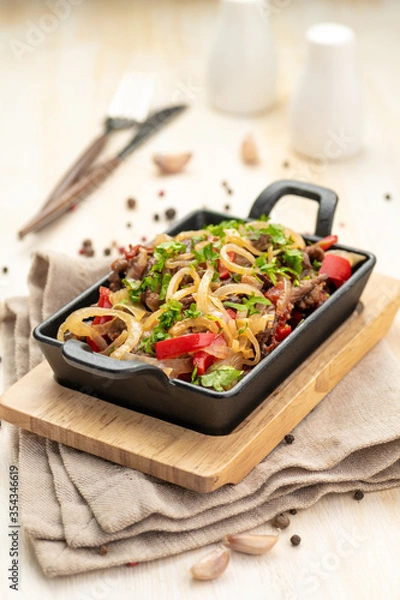 Fototapeta Roast meat with vegetables in a cast iron skillet on a wooden background and a linen napkin.