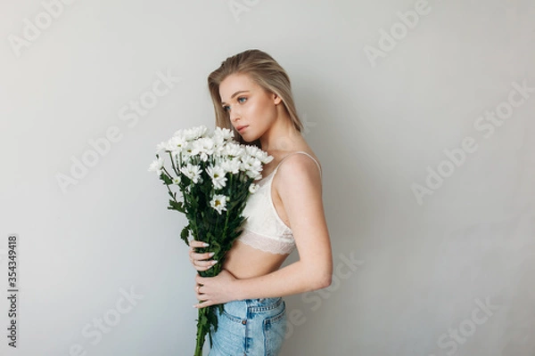 Fototapeta A beautiful girl with blonde hair in underwear is holding a bouquet of daisies. Blonde and a bunch of daisies for mother's Day