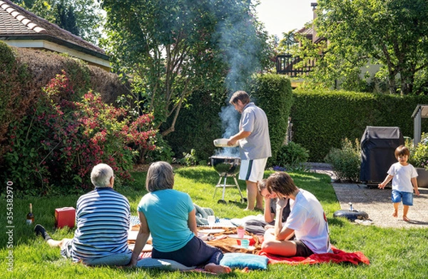 Fototapeta Big family having picnic and barbecue sitting on grass in garden at home at bright sunny day. Weekend leisure lifestyle activity. Alternative holidays during quarantine.