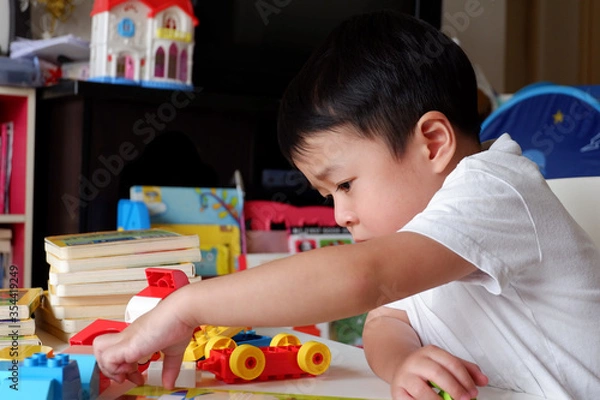 Obraz An Asian boy is playing a toy on a white table.