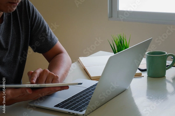 Obraz An Asian man uses a laptop at home while sitting at a wooden table. Man hands typing on a notebook keyboard.