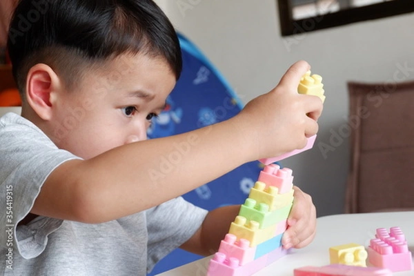 Fototapeta Close up of child's hands playing with colorful plastic bricks at the table. Toddler having fun and building out of bright constructor bricks. Early learning. stripe background. Developing toys
