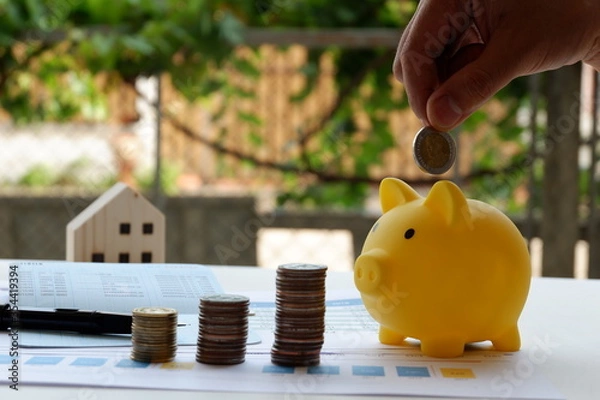 Obraz Inserting a coin into a piggy bank , Hand puts a coin in the piggy bank on nature background