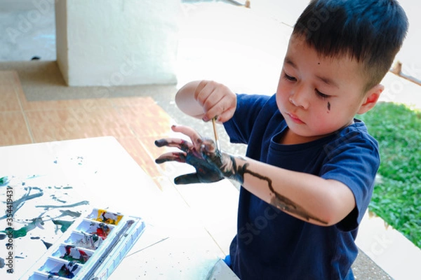 Obraz Asian little boy with hand painted in colorful paints, workshop for children concept. Leaning and education of kid at home.