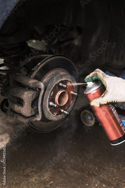Fototapeta A car service worker with gloves splashes brake discs on a passenger car with grease. Auto to replace the wheels