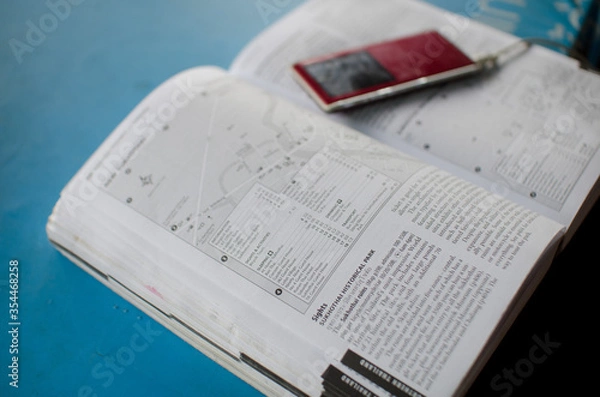 Fototapeta Travel guide book on table with electronic device