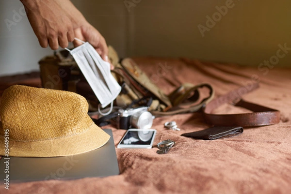Fototapeta      Travel idea with a hat and bag and a laptop with a hand picking a mask