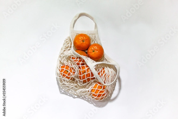 Fototapeta Fresh mandarines in a string bag, eco-friendly product on a light  background. No plastic, only natural materials and natural products. Concept of life without plastic.