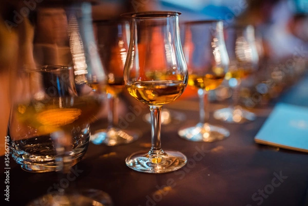 Fototapeta Glasses with brandy stand in a row. Blurred background, warm tinted. Tasting glasses with aged french cognac brandy