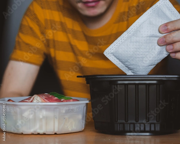 Obraz Man cooking self heating hot pot can order to home delivery ready to eat by heat from self heating pad which contains noodle,Sliced wagyu marbled beef,Cantonese vegetables,fried shrimp ball,mushroom.