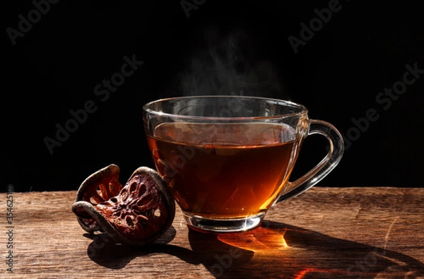 Fototapeta The Bael fruit juice in a glass and dried Bael fruit placed on the wooden floor with black background.Drinking Bael fruit juice in the morning will help the body to refresh.
