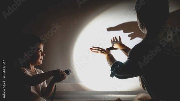Fototapeta Toned photo of young mother and little boy playing in theater of shadows before going to sleep at night