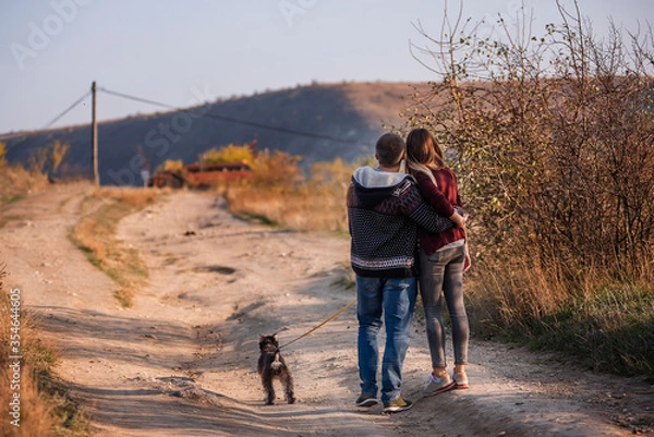 Fototapeta A young couple stands with their backs to the camera and looks to their bright future against a clear blue sky. A happy family travels around the country on their weekends in search of beautiful place