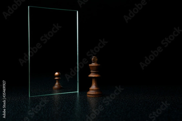 Obraz the king is reflected in the mirror as a pawn on black background. underestimation of their abilities