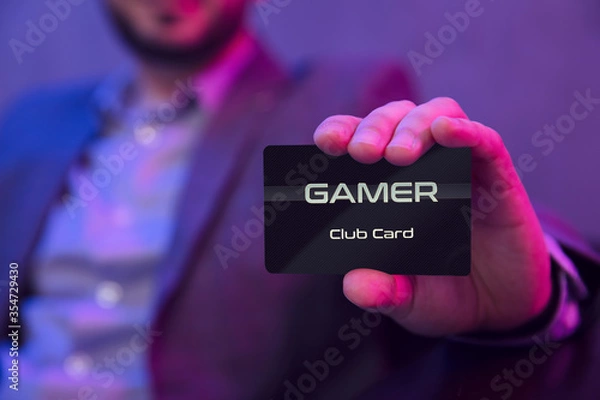 Fototapeta Man's hand holds gamer clubcard. Gentleman in suit holds gamer membership club card in his hand